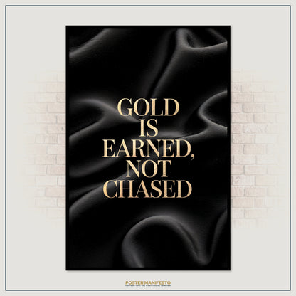 Poster with gold text 'Gold is earned, not chased' on a black background, framed against a brick wall.